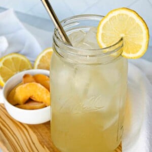 A large mason jar full of iced peach green tea lemonade, garnished with lemon.