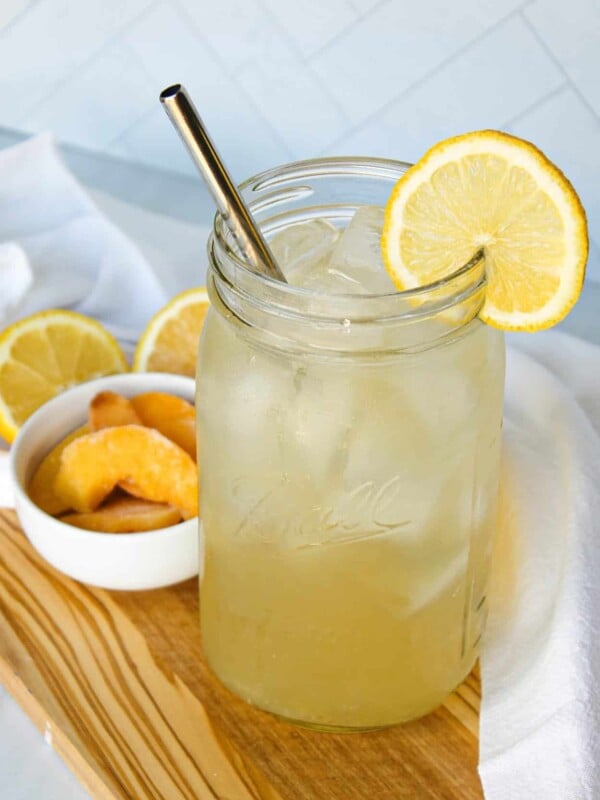 A large mason jar full of iced peach green tea lemonade, garnished with lemon.