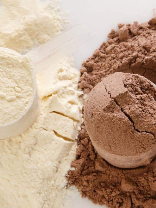 A scoop of collagen powder side by side with a scoop of chocolate protein powder.