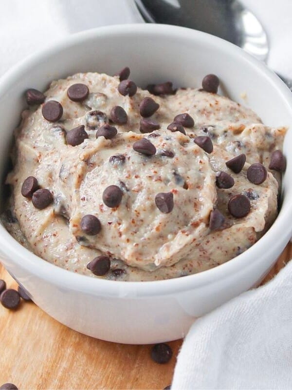 A small white bowl of cottage cheese cookie dough on a wooden board with a spoon.