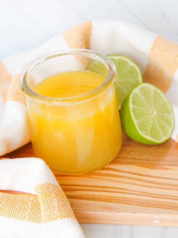 A small jar of honey lime vinaigrette with two lime halves on a wooden board.