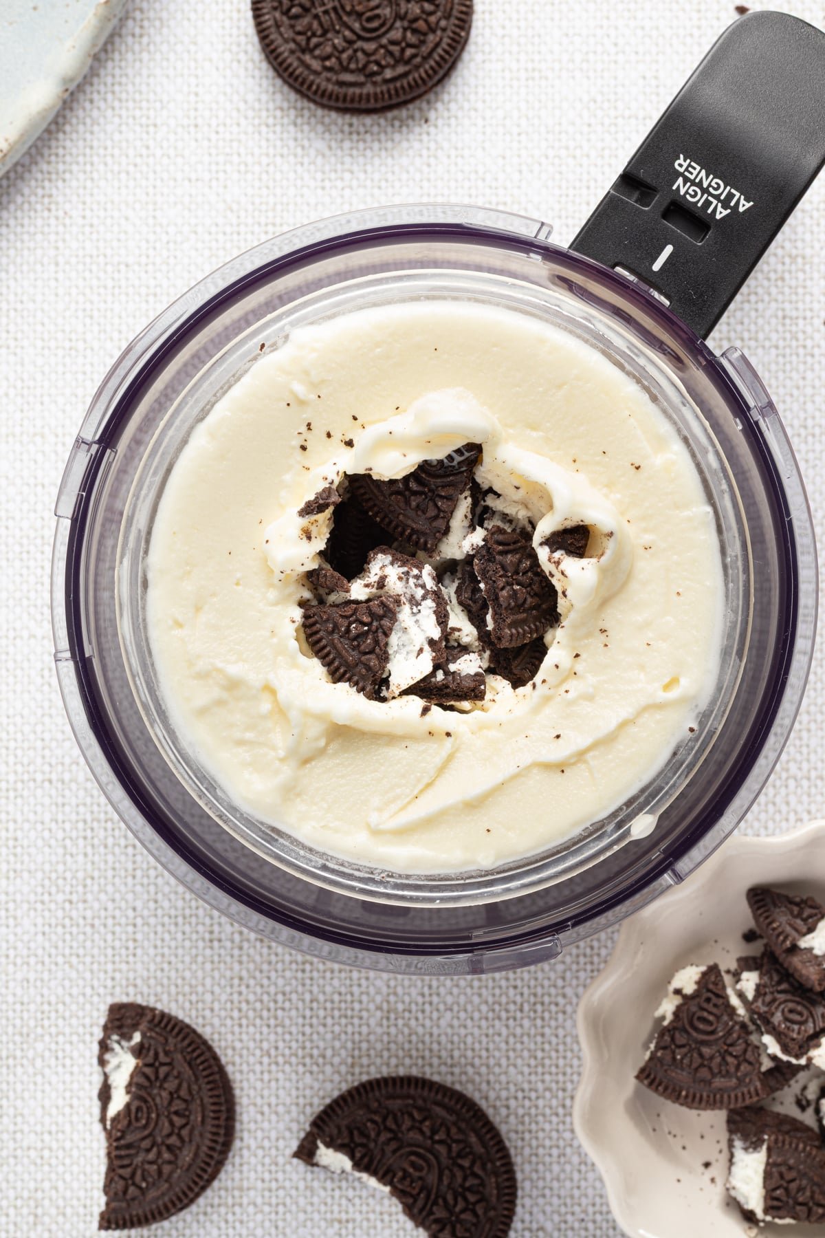 Oreos being added to a ninja creami container with vanilla ice cream.