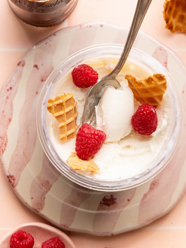 The Ninja Creami frozen yogurt in the creami container with pieces of ice cream cone and three raspberries.