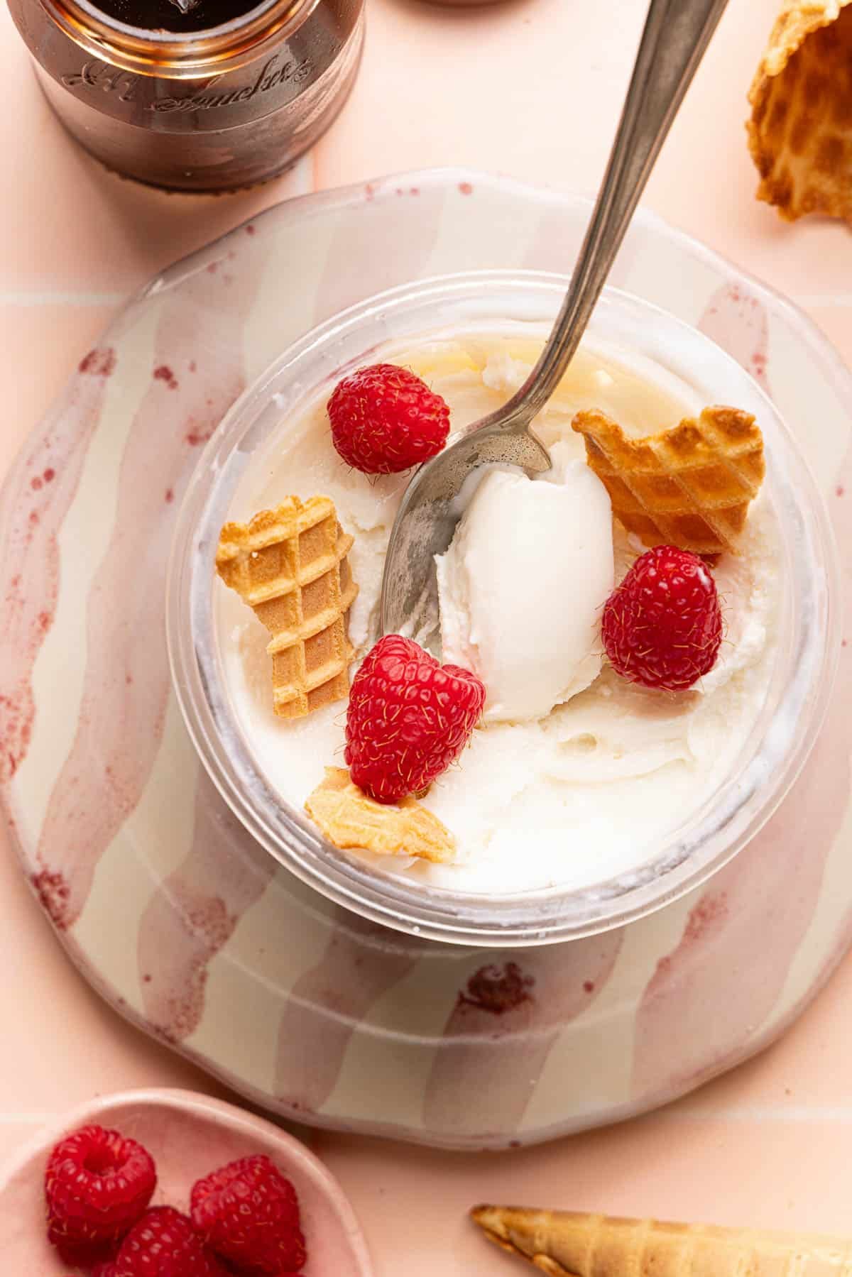 The Ninja Creami frozen yogurt in the creami container with pieces of ice cream cone and three raspberries.