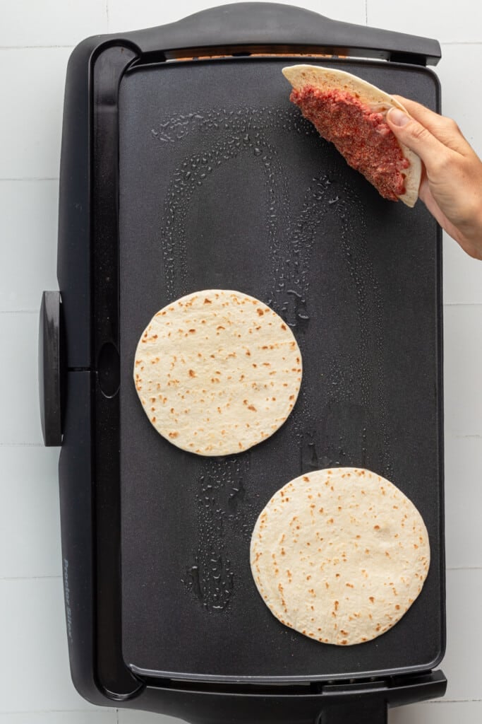Big Mac tacos being put onto a griddle with the ground beef side face down.