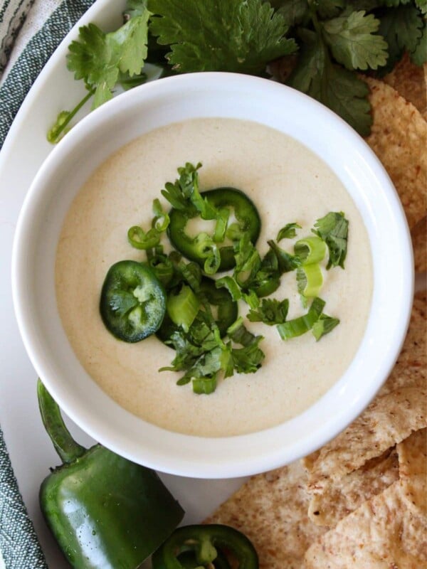 Cottage cheese queso in a white bowl topped with chives, cilantro and jalapeños.