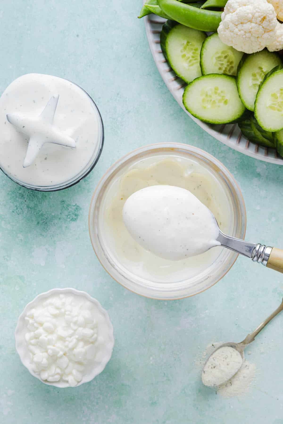 A spoon with a spoonful of cottage cheese ranch dip over the blender bowl to show the texture.