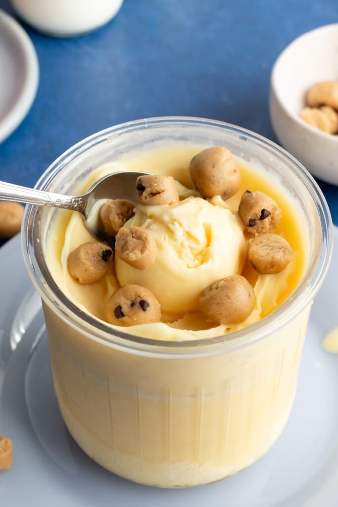 Vanilla protein ice cream in a Ninja Creami pint container topped with cookie dough pieces.