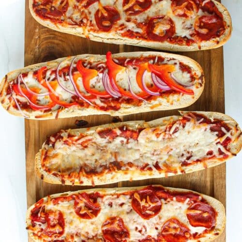 Four pizza boats lined up on a sheet pan baked with different toppings.