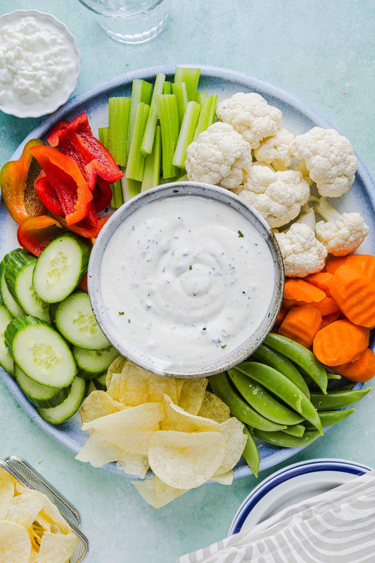 Cottage cheese ranch dip in a bowl on a vegetable platter with sliced cucumbers, red bell pepper, celery, cauliflower, carrots, snap peas, and chips.