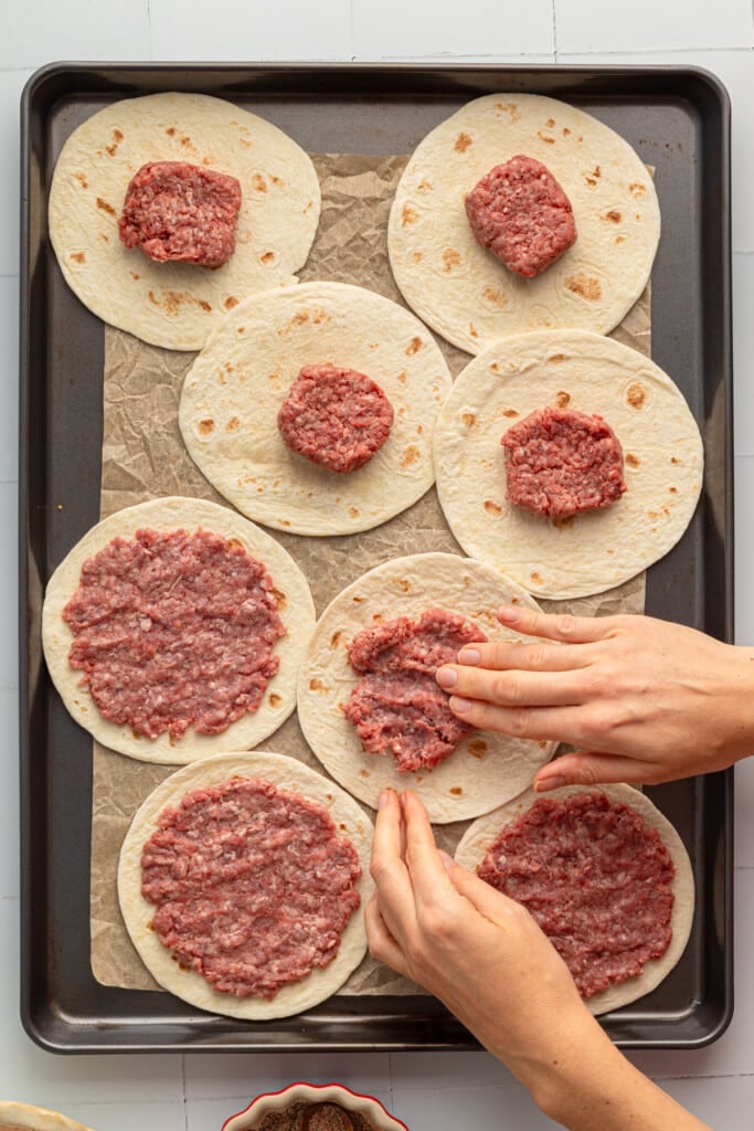 small ground beef patties being pressed onto tortillas for Big Mac smash burger tacos.