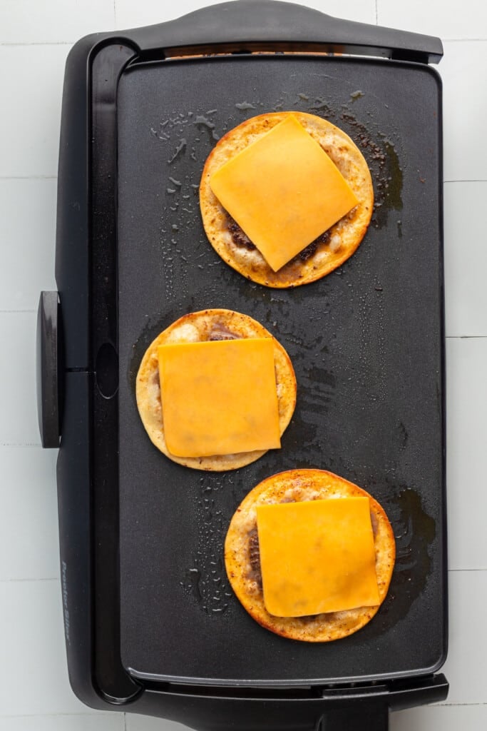 Cheese added to Big Mac tacos on a griddle.