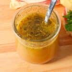 A small glass jar of italian submarine dressing with a spoon and sandwiches.