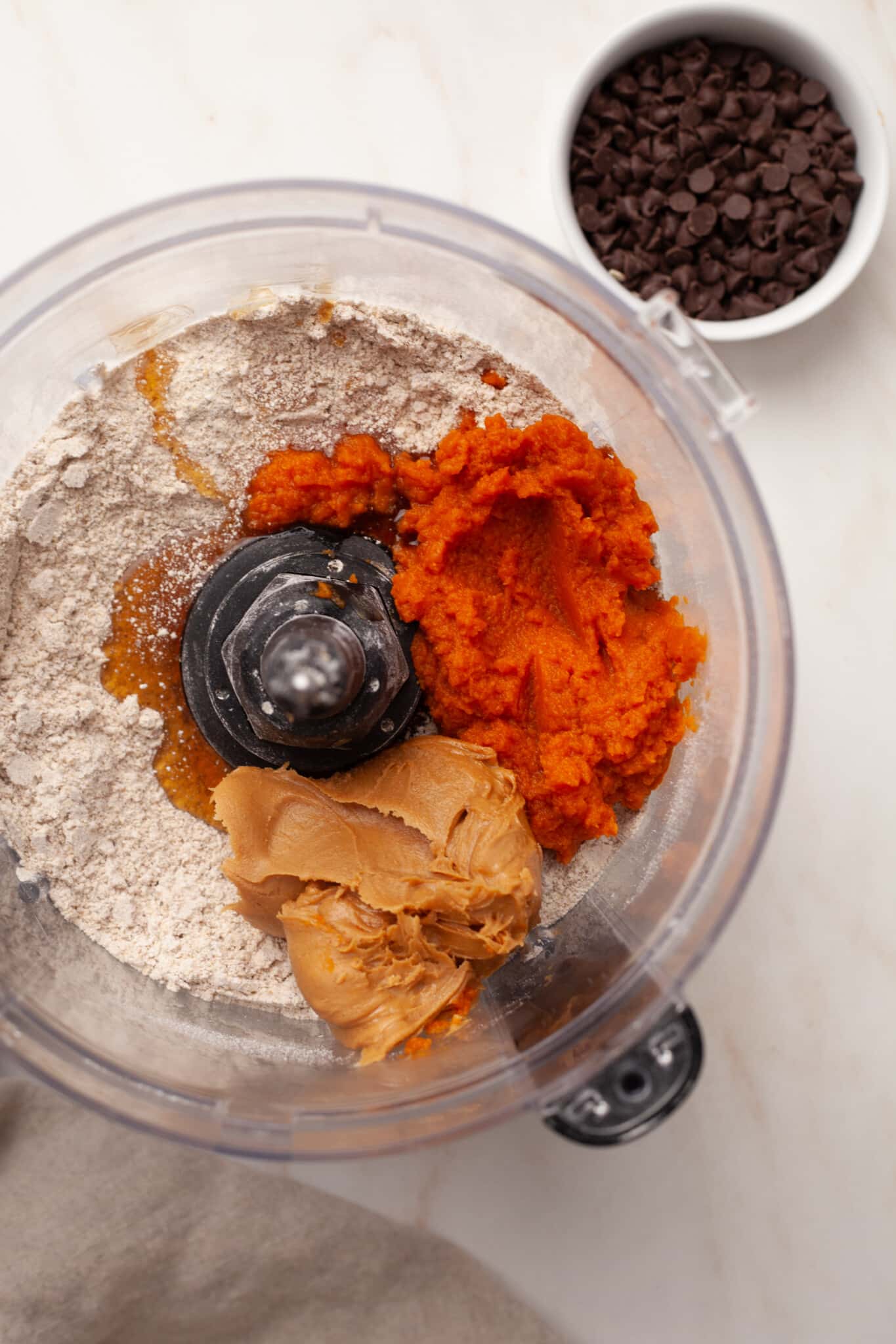 Oats, pumpkin, peanut butter and other ingredients for pumpkin protein balls in a food processor.