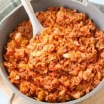 A skillet full of unstuffed cabbage roll with a large serving spoon.