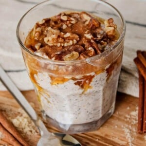 Maple brown sugar overnight oats in a glass topped with walnuts, cinnamon and maple syrup.