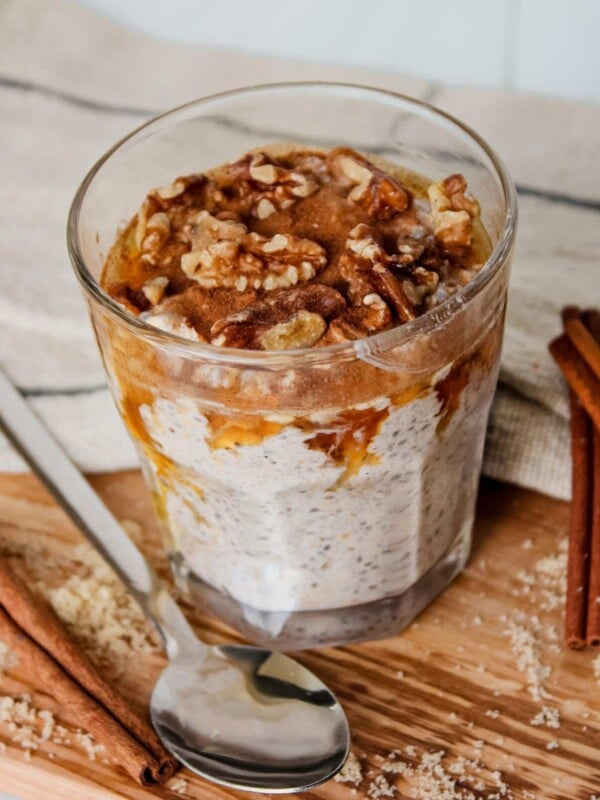 Maple brown sugar overnight oats in a glass topped with walnuts, cinnamon and maple syrup.