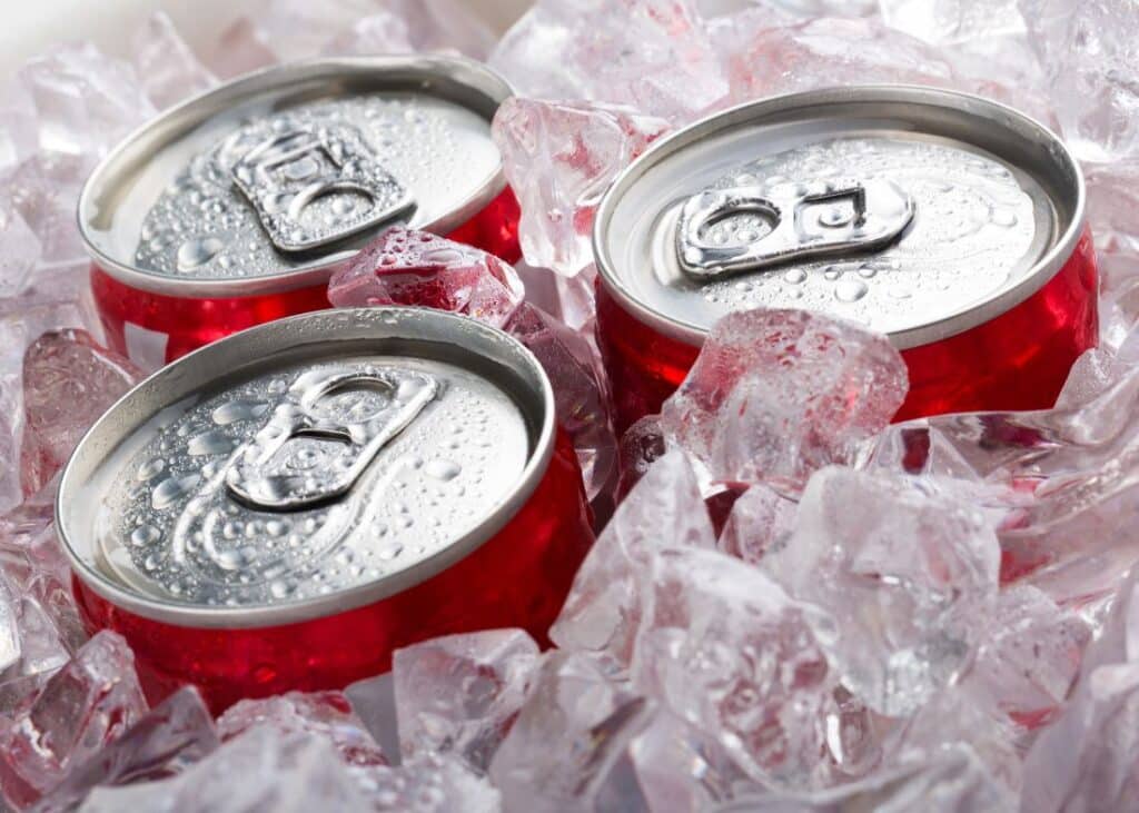 Three cans of soda in ice with just the tops showing.