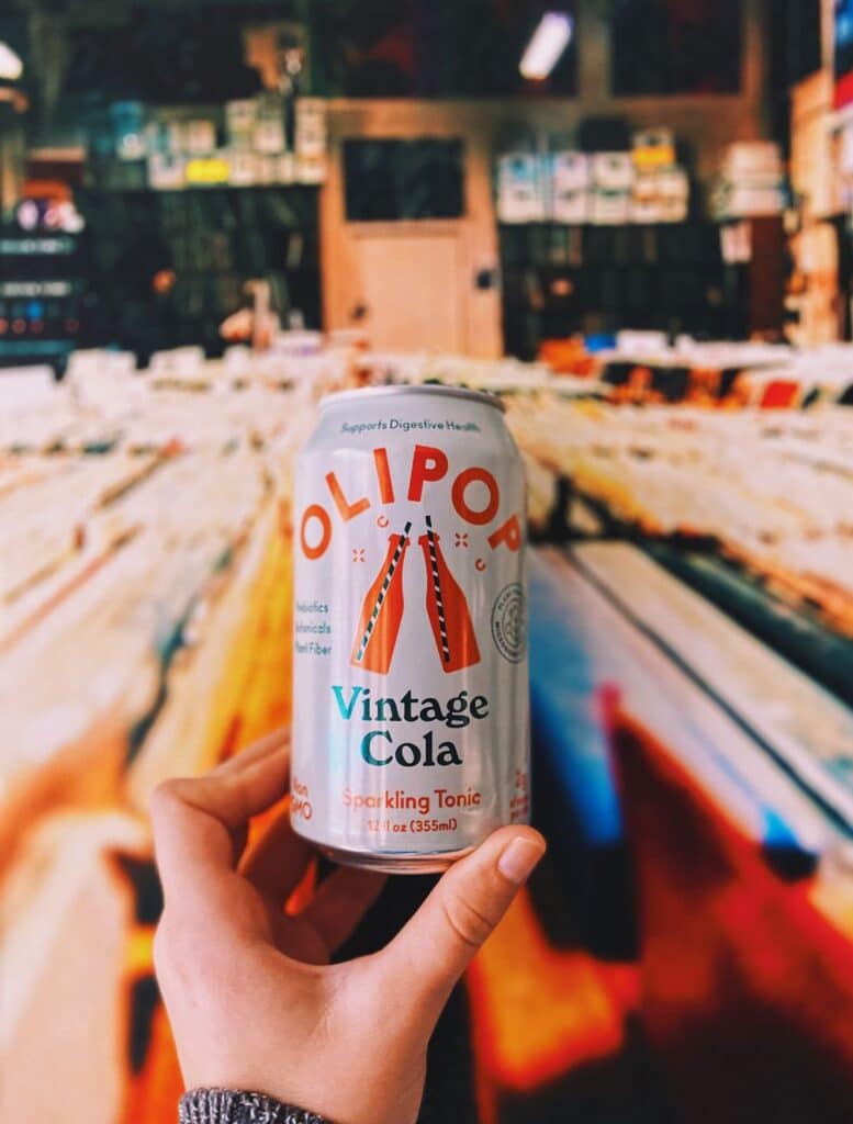 A person holding a vintage cola flavored Olipop soda in a record store. 