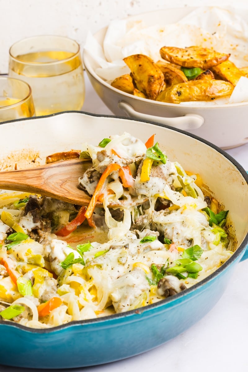 Philly cheesesteak casserole being scooped out with a wooden spoon.