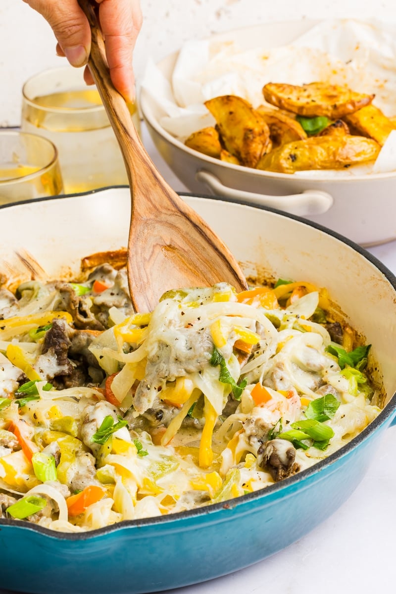 Philly cheesesteak casserole being scooped out with a wooden spoon.