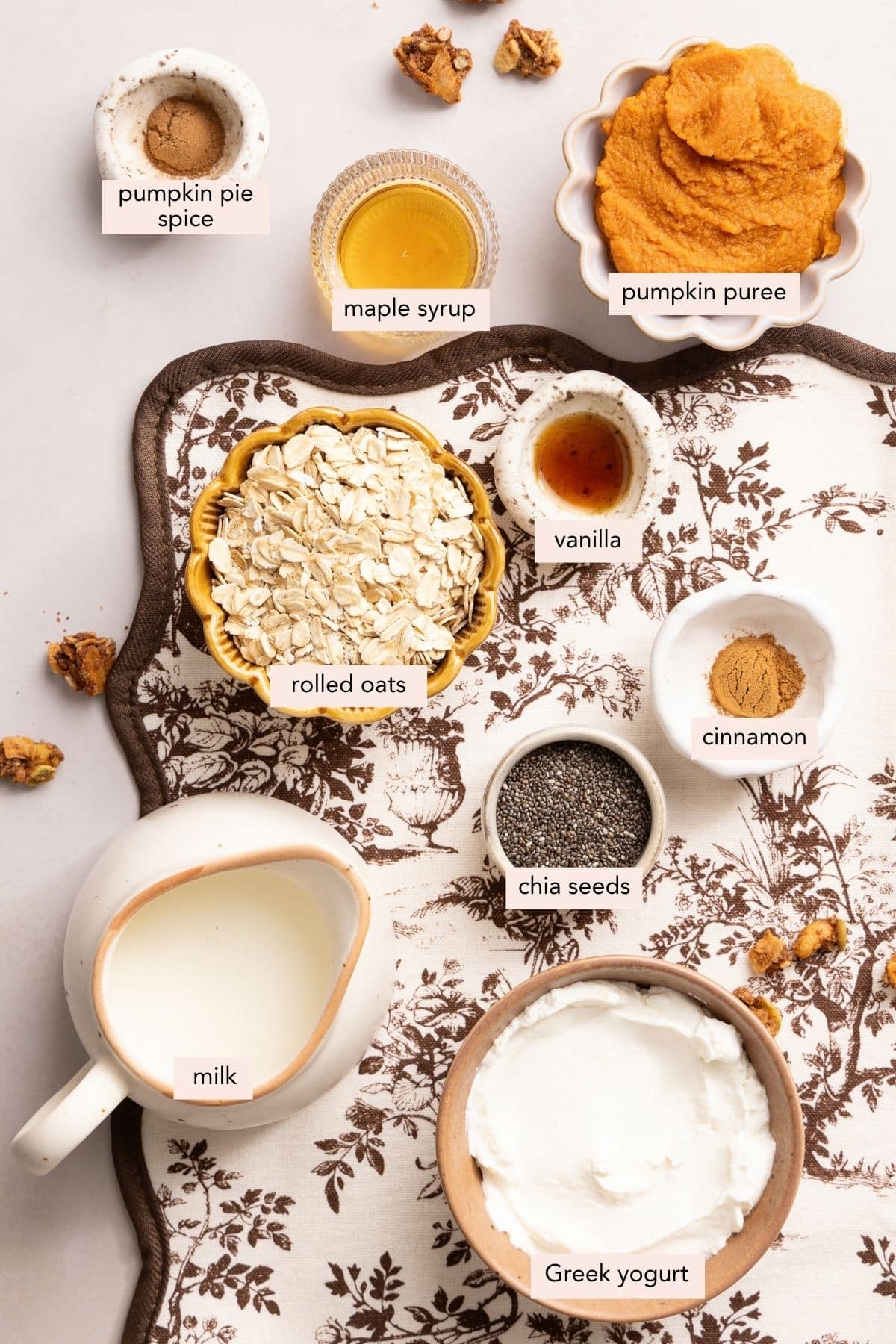 All of the ingredients for pumpkin overnight oats in bowls on a countertop.
