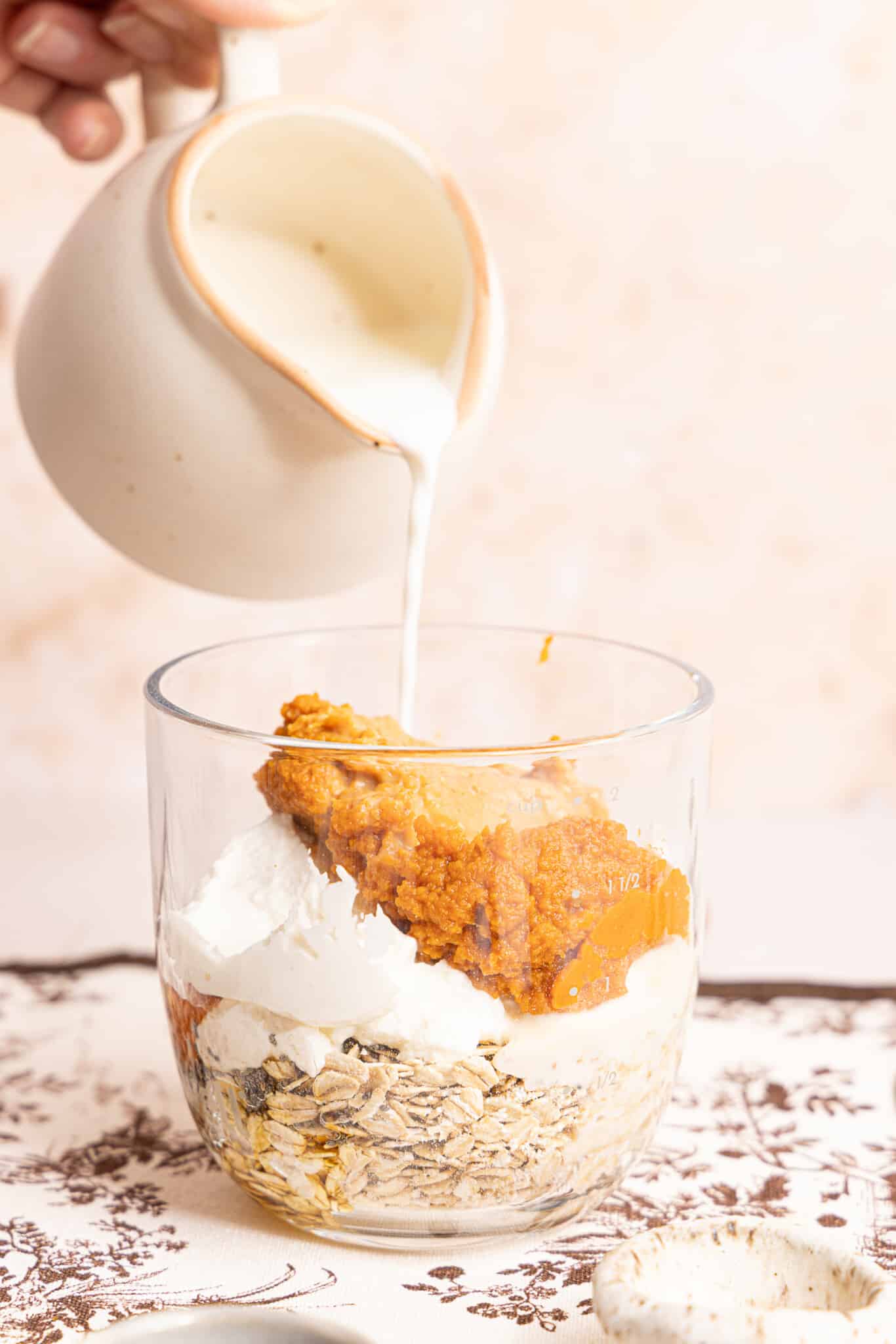 A hand pours a glass of milk into the remaining ingredients for the overnight oats in a jar.