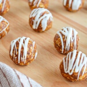 Pumpkin protein balls drizzled with white chocolate arranged on a wooden board.