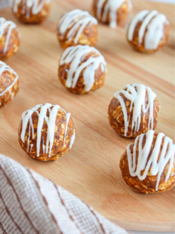 Pumpkin protein balls drizzled with white chocolate arranged on a wooden board.