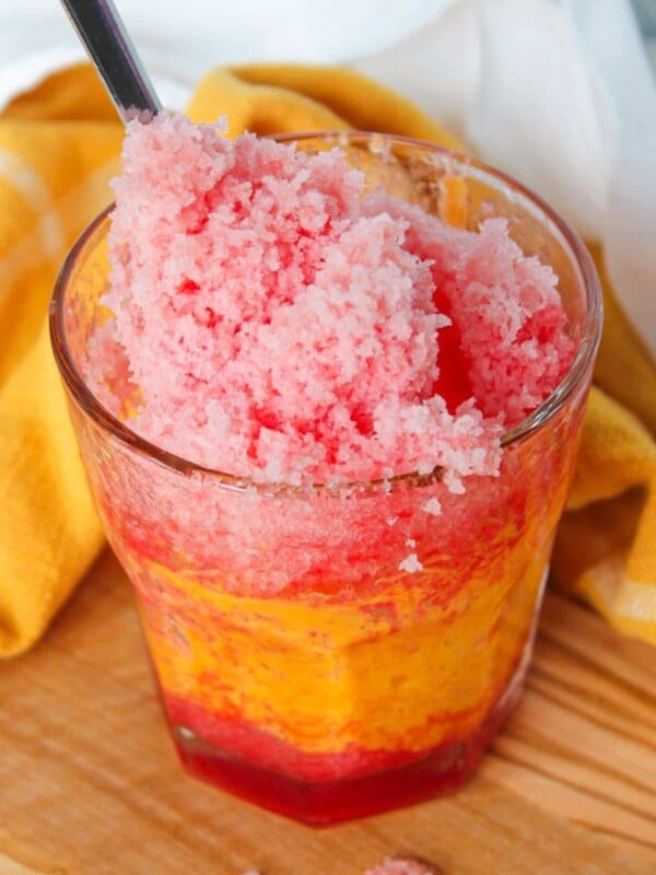 Frozen fruit shaved ice in a clear glass with a spoon.