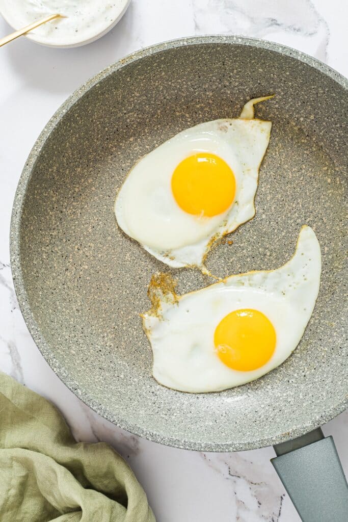 Two eggs being fried in a pan.