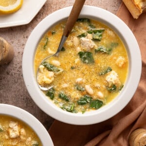 A bowl of chicken cauliflower soup on a countertop with a spoon.