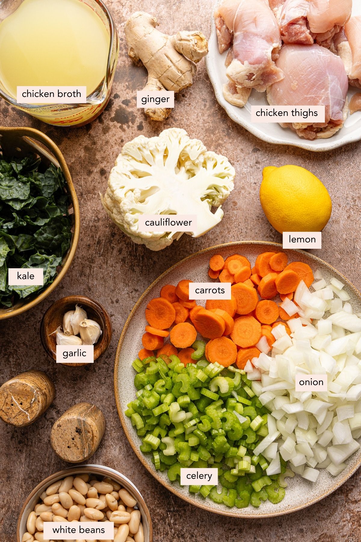 All of the ingredients for cauliflower chicken soup in bowls on a countertop.