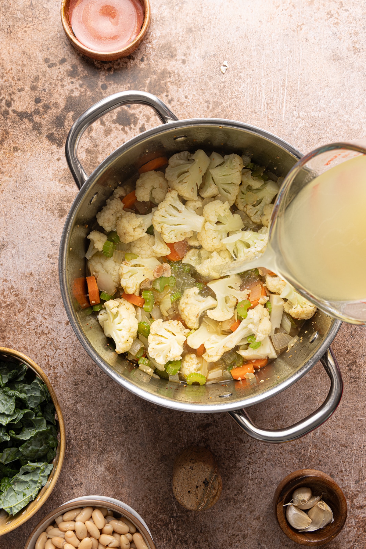 The broth pours out of a measuring cup into the pot with the softened vegetables.