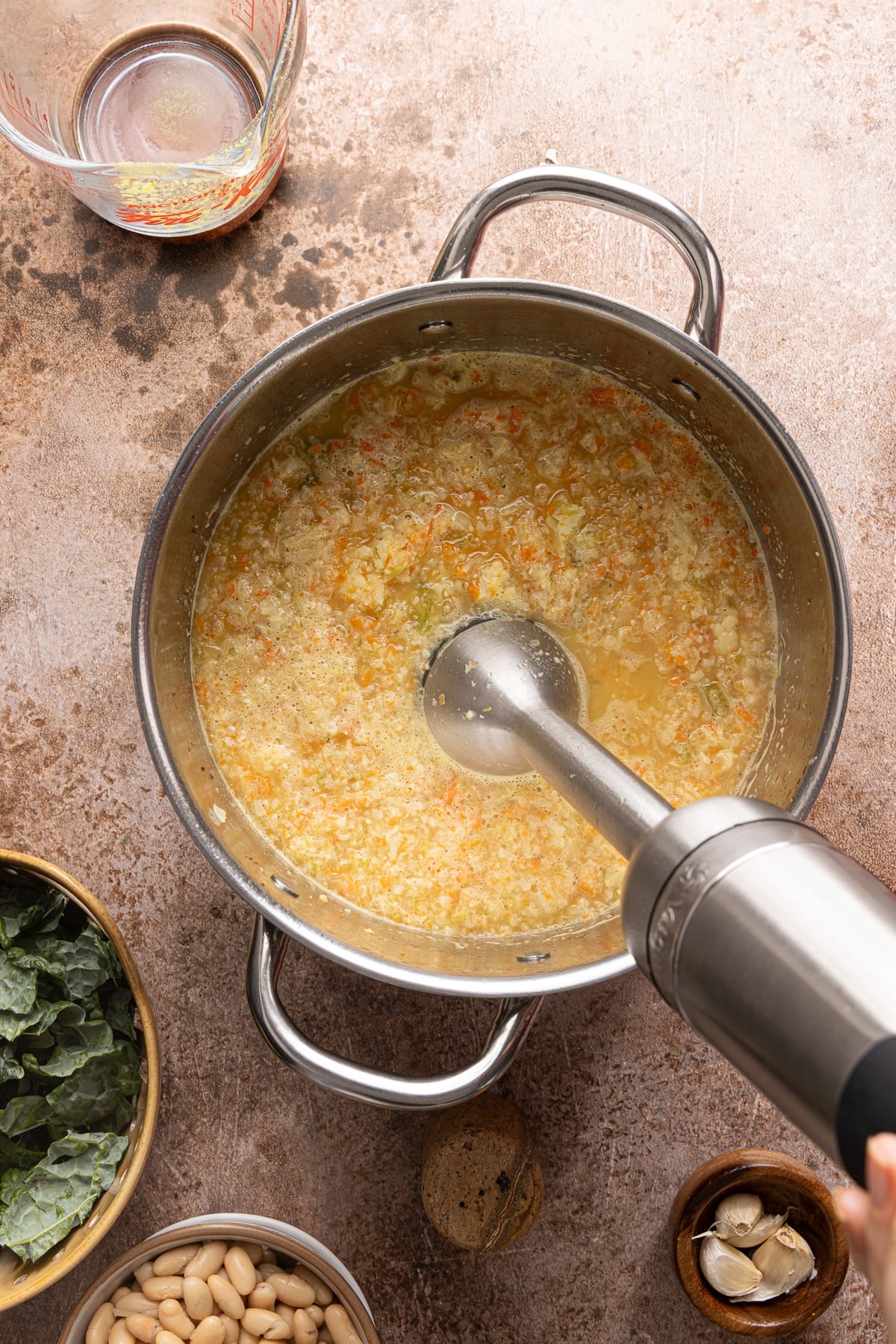 An immersion blender blends the vegetables and broth in the pot.