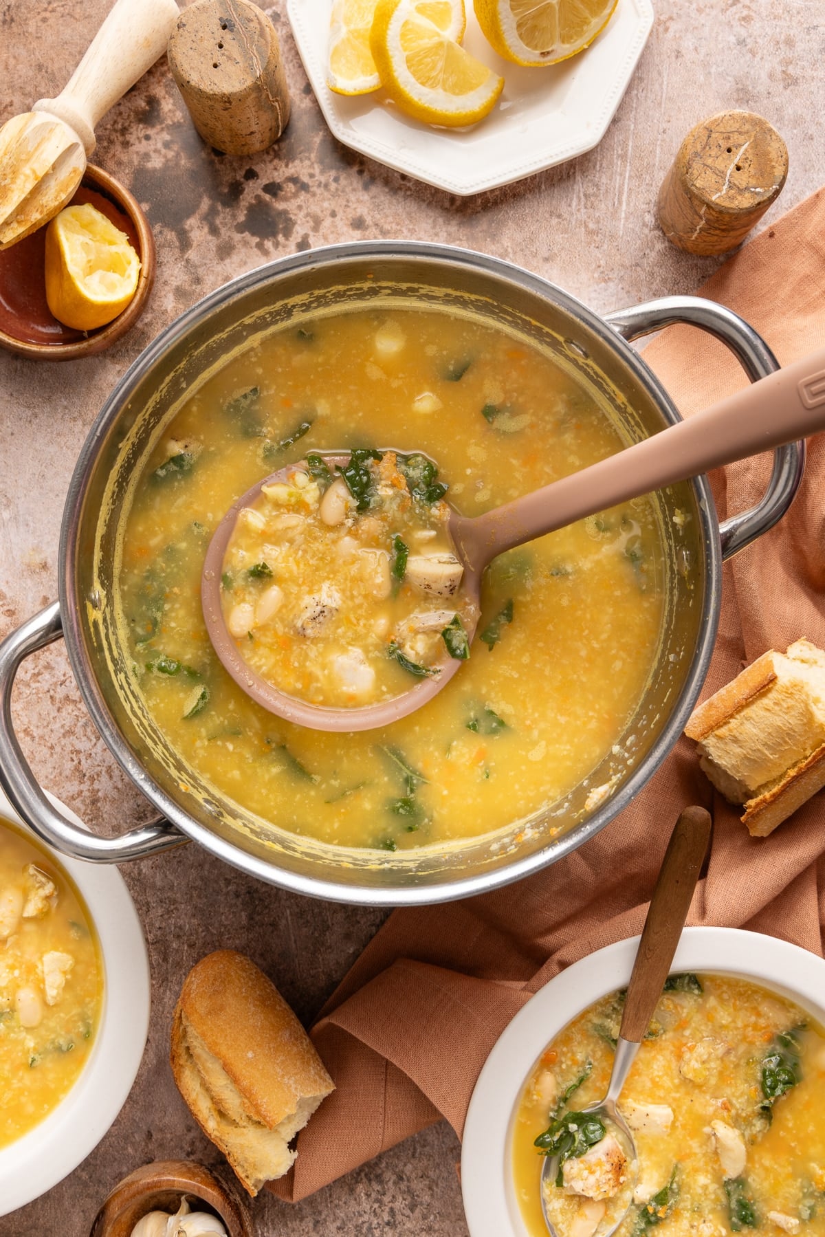 A ladle scoops some of the cooked chicken cauliflower soup from the pot.