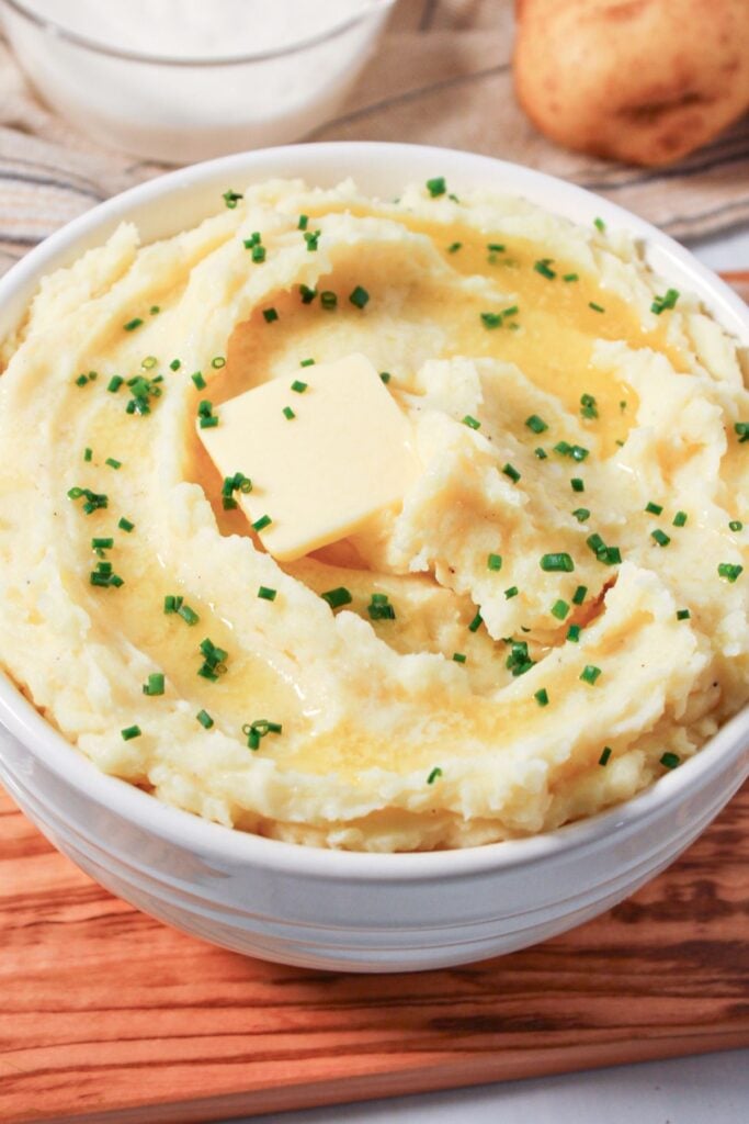 Cottage cheese mashed potatoes in a white bowl with butter and chives.