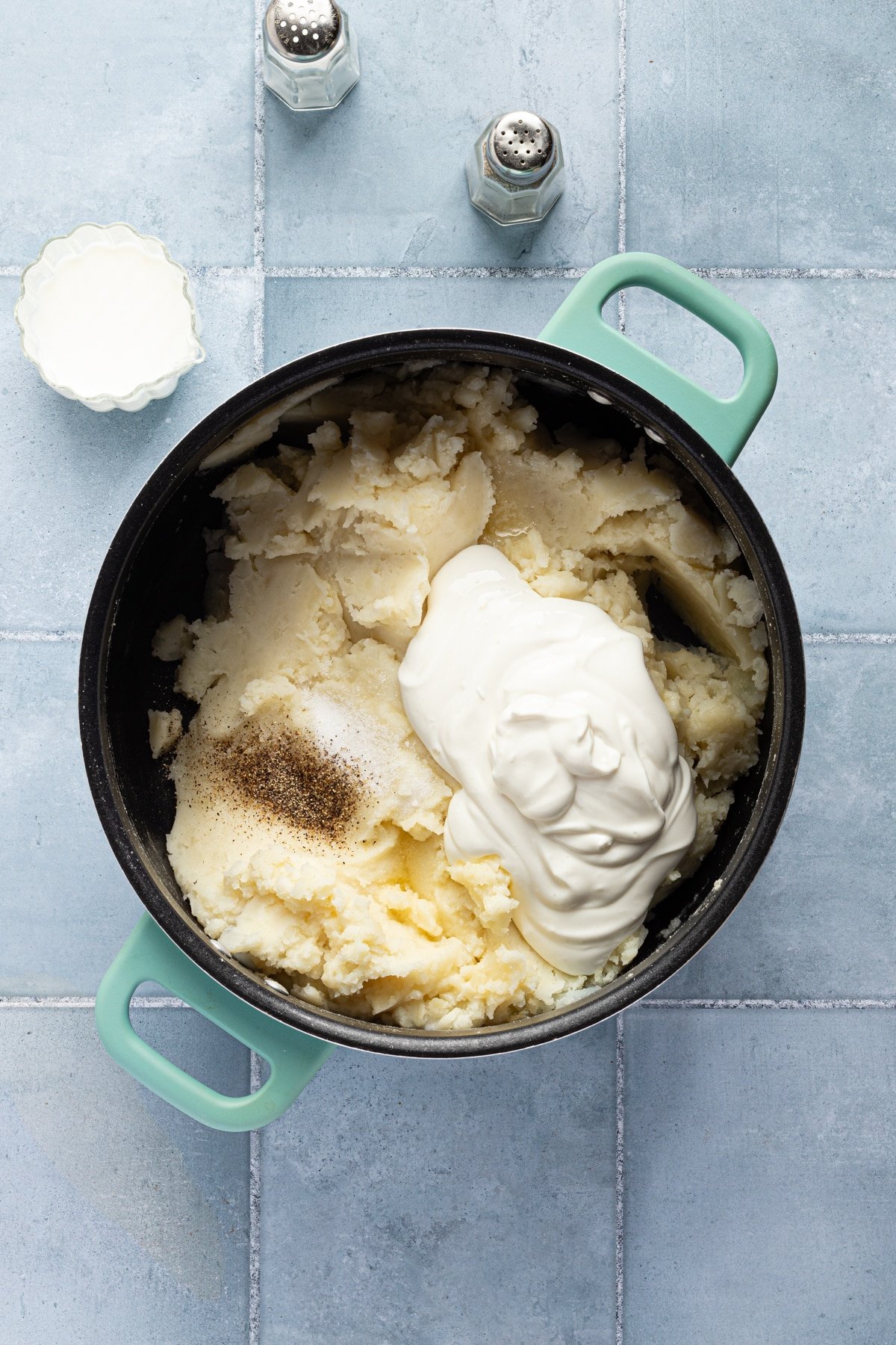 Butter, cottage cheese, salt and pepper being added to mashed potatoes and garlic.
