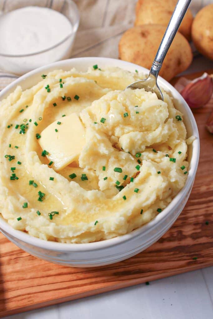 A bowl of cottage cheese mashed potatoes with butter and chives with a spoon.