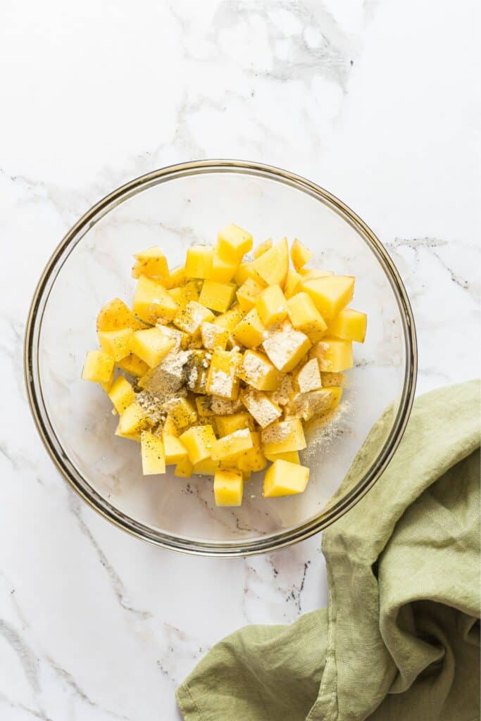 A clear bowl with cubed potatoes and seasoning on top.