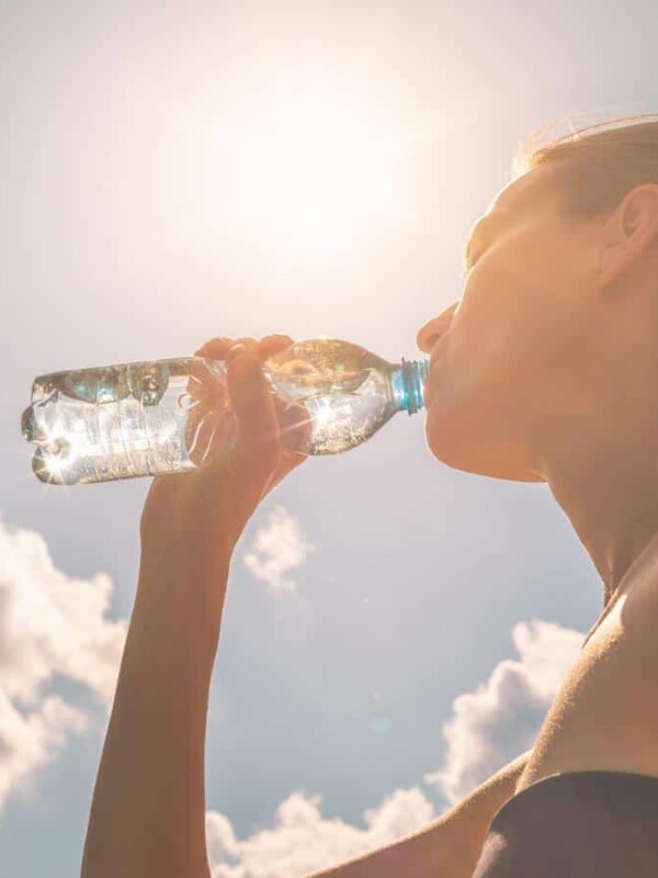 A woman taking a drink of a water bottle with a blue sky in the background.