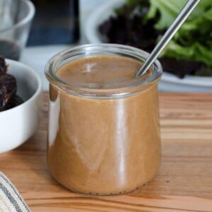 A clear glass jar of balsamic date dressing with a spoon.