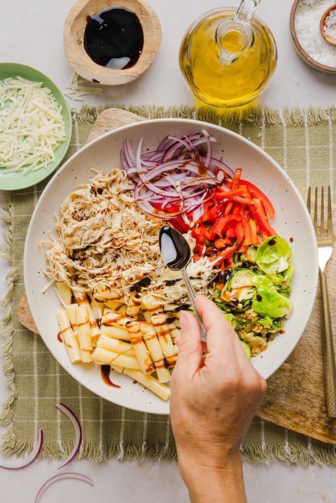 A brussels pasta bowl being assembled and balsamic glaze being drizzled on top.