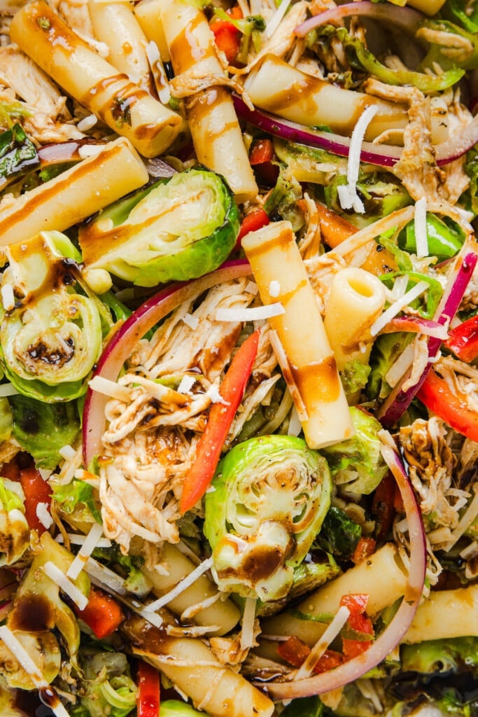A close up shot of a brussels sprout pasta salad bowl in a bowl drizzled with balsamic glaze.