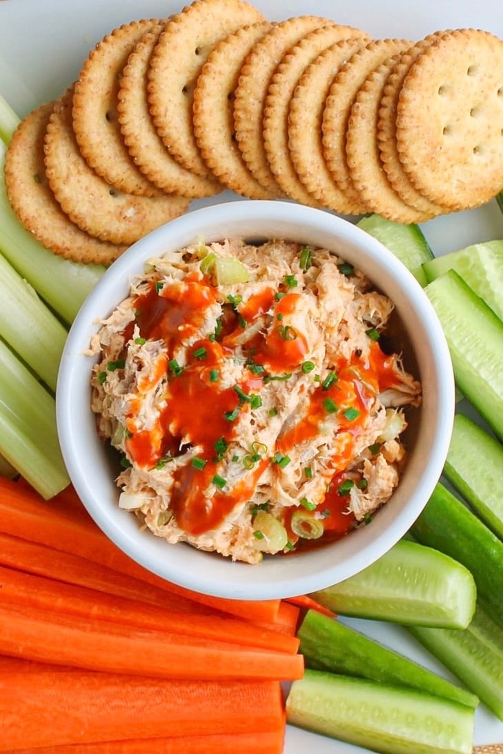 Buffalo chicken salad in a white bowl with crackers and sliced veggies.
