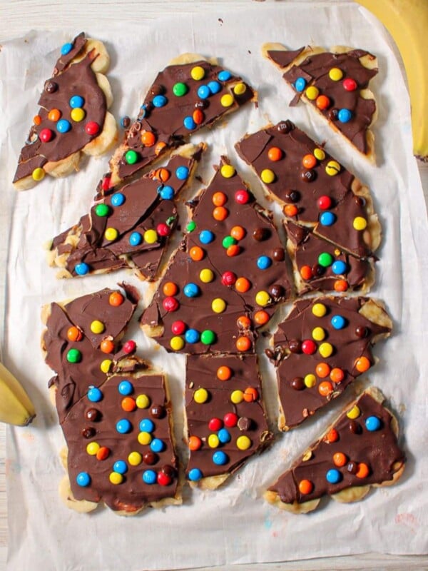 Chocolate banana bark sprinkled with mini M&Ms broken into pieces on parchment paper.