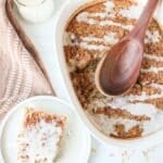 A white casserole dish with cinnamon roll oatmeal bake drizzled with a cinnamon roll glaze with a slice next to it on a plate.