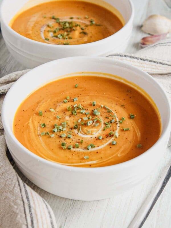 Two white bowls of honeynut squash soup garnished with sour cream and chives.