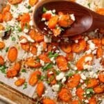 A sheet pan with sliced roasted carrots made with hot honey and sprinkled with feta cheese, chives and parsley.