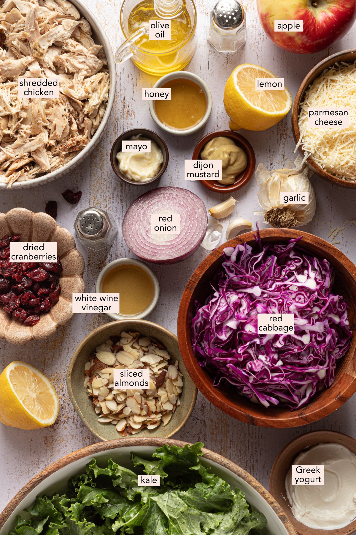 Ingredients for kale chicken salad in bowls on a countertop with labels.